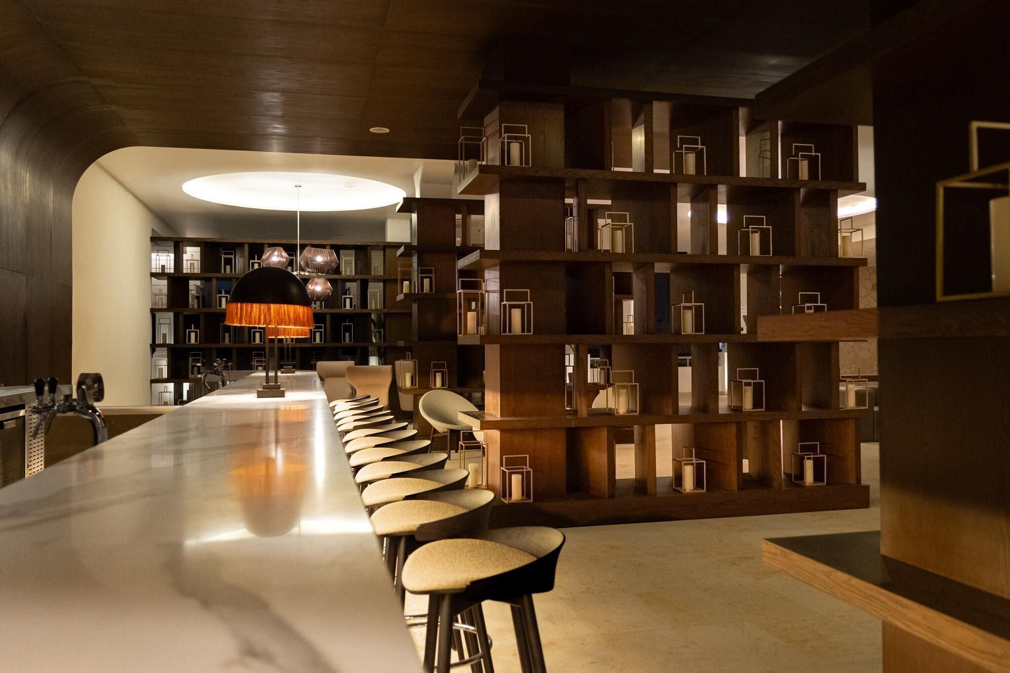 A modern bar area with a long counter, multiple stools, and a central hanging light fixture.
