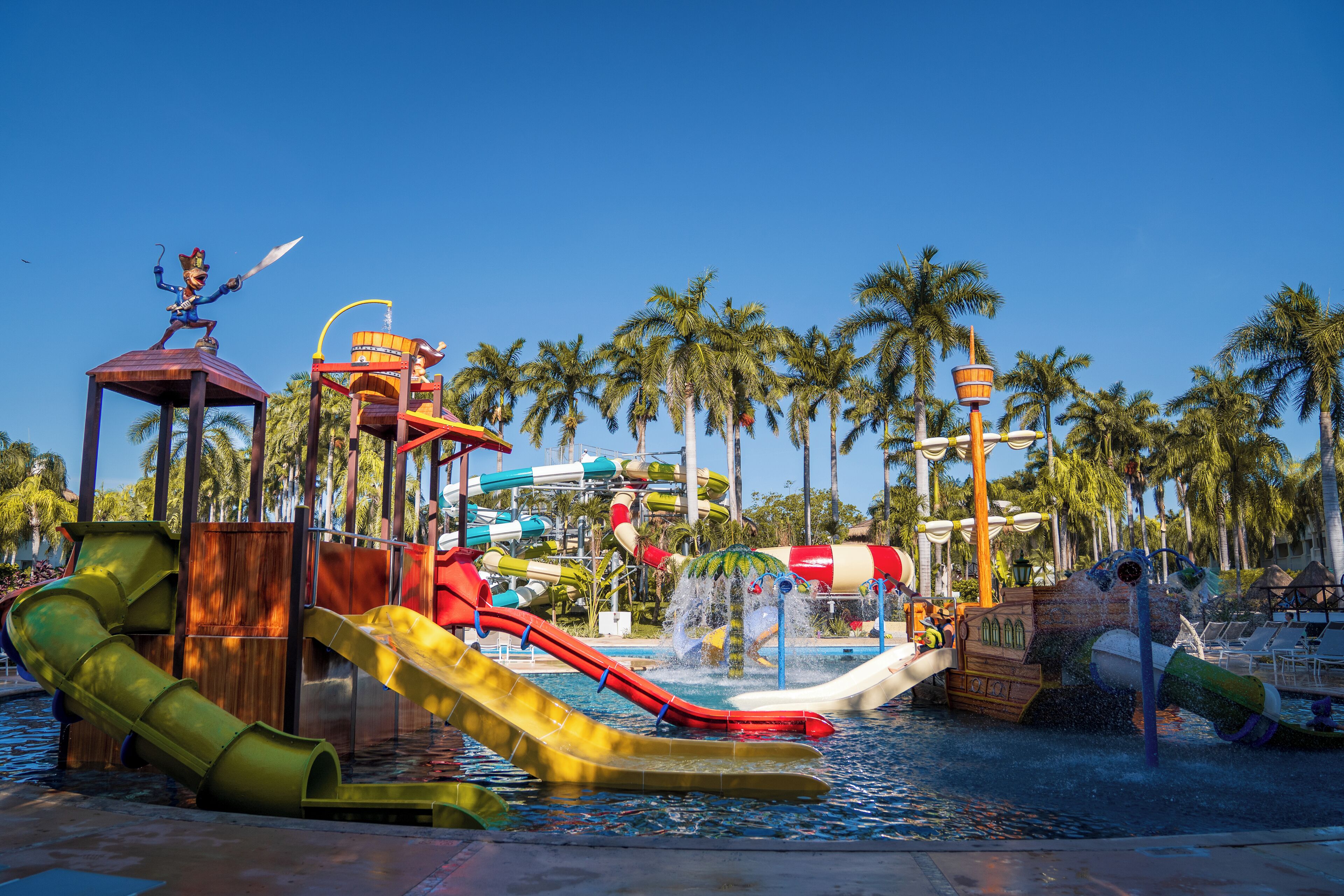 A water park with slides, a wooden boat ride, and palm trees.