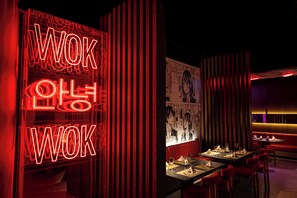 L’intérieur d’un restaurant, avec des enseignes au néon rouge, des lambris en bois et une fresque murale.