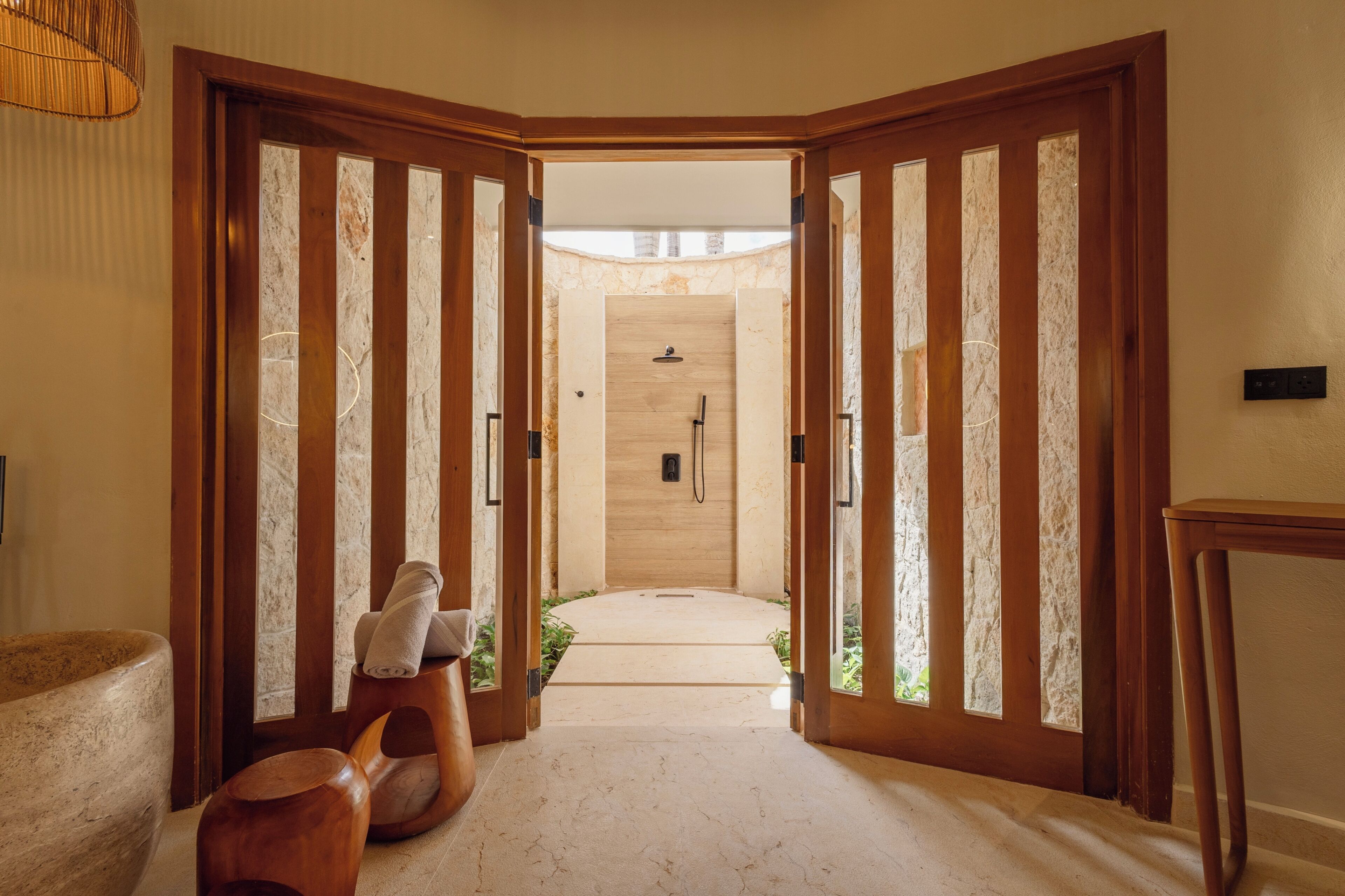 A hallway leading to a bathroom with a shower, wooden doors, and a stone wall.