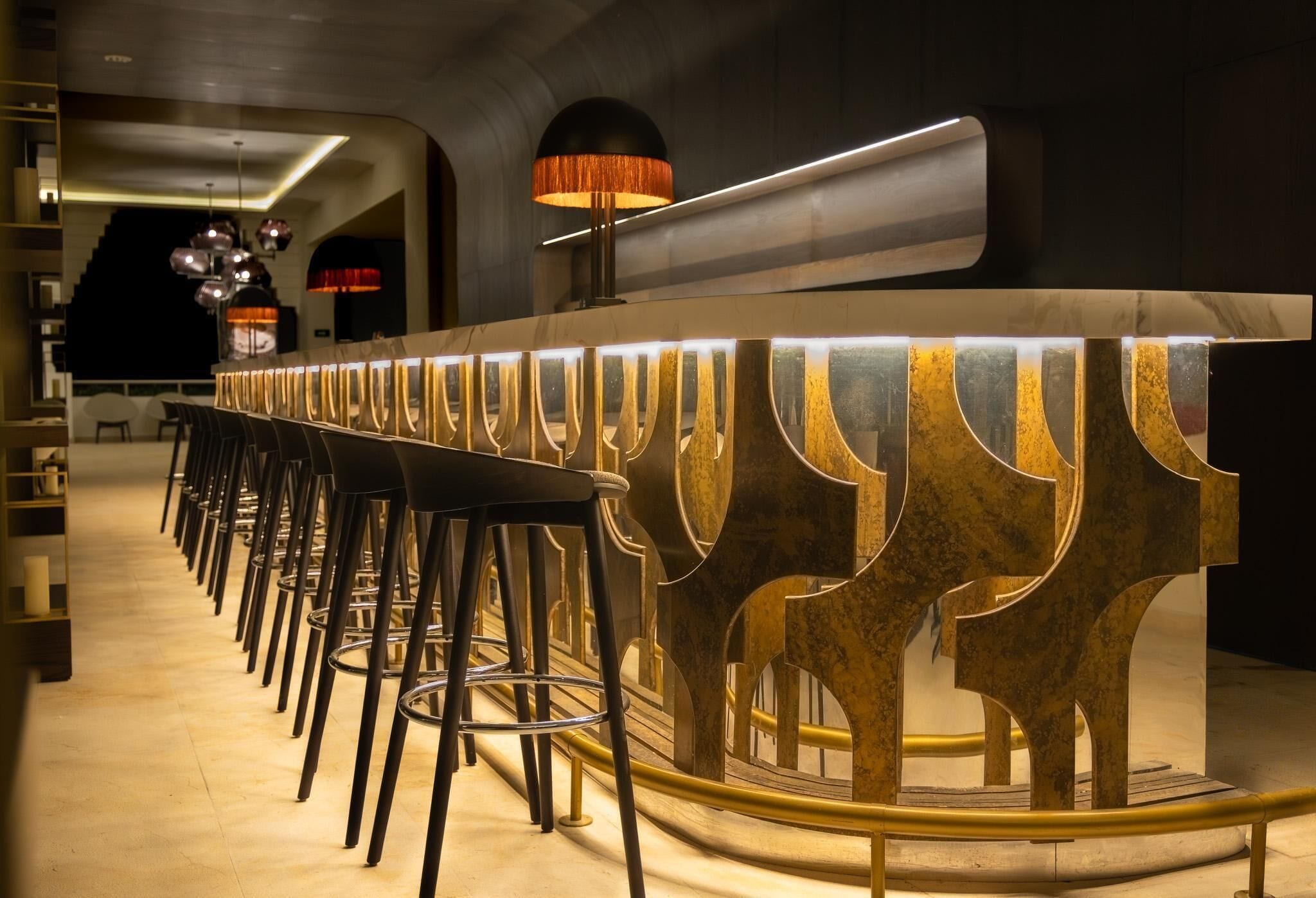 A bar area with a long counter, multiple stools, and a distinctive gold and white patterned design.