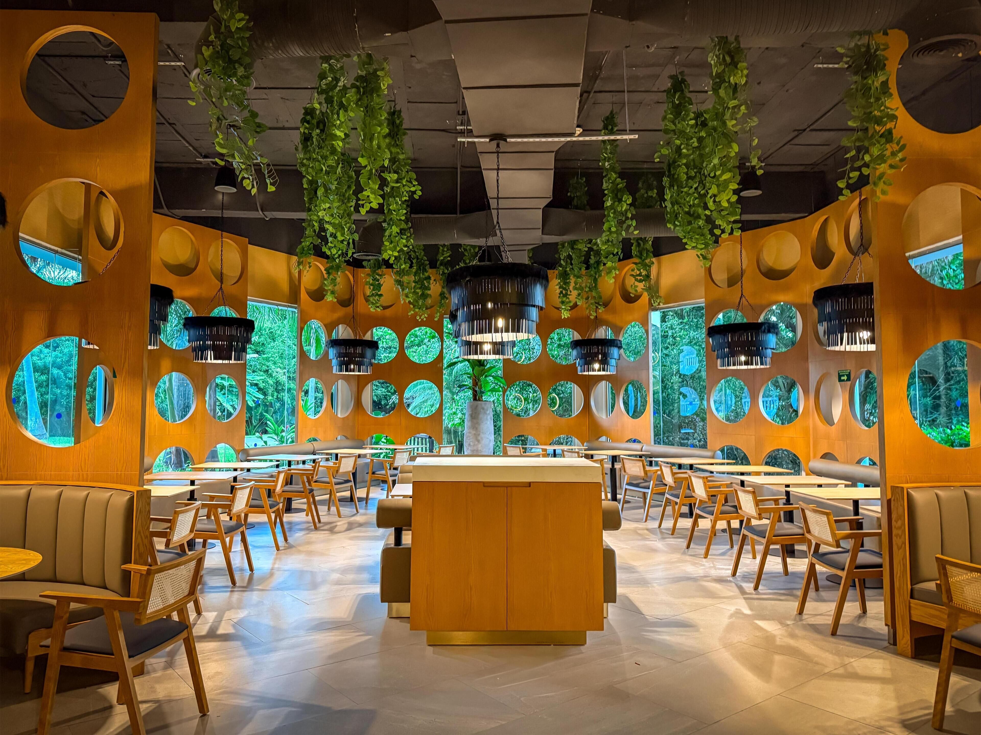 A modern restaurant interior with round mirrors, wooden furniture, and hanging plants.