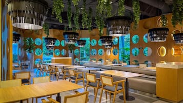 Un restaurante moderno con mesas y sillas de madera, plantas colgantes y decoraciones circulares en las paredes.