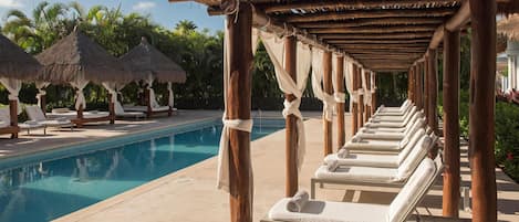 Un área junto a la piscina con sillones de descanso y sombrillas de paja.