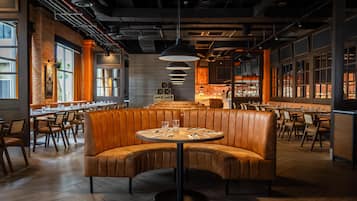 Un restaurant doté d’un espace de sièges central avec des banquettes, de longues tables communes et un plafond au design industriel moderne.