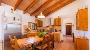 Eine Küche mit Holzausbau, einem Edelstahlkühlschrank, einem Esstisch aus Holz mit Stühlen und einer Hängeleuchte.