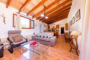 A spacious living area with a sofa, armchair, and glass coffee table. A kitchen area is visible in the background.