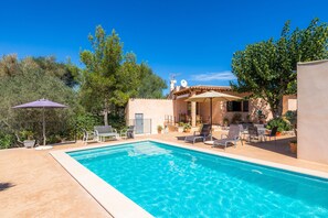 A swimming pool with lounge chairs, a patio area, and a building with a tiled roof.