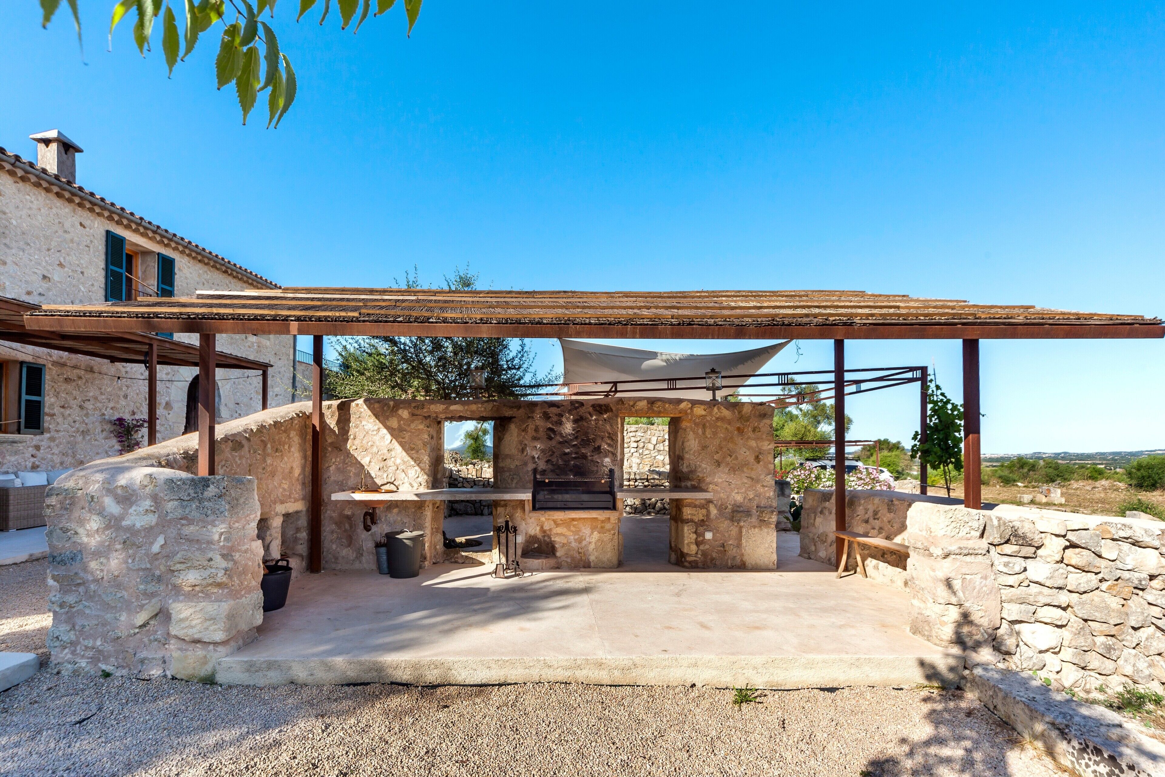 An outdoor kitchen area with stone walls, a pergola, and a view of the surrounding landscape.