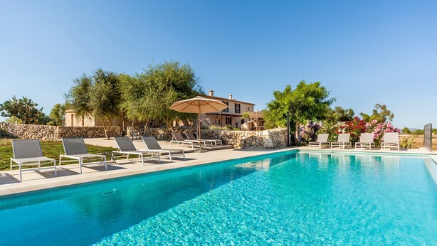 Une piscine entourée de murs de pierre et de verdure, avec des chaises longues et un parasol.