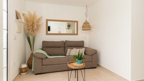 Een woonkamer met een bruine bank, een rond bijzettafeltje met een plant, een grote spiegel en een hanglamp.