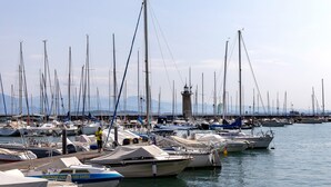 Un puerto deportivo con numerosas embarcaciones amarradas, un faro al fondo y una persona de pie en un bote.