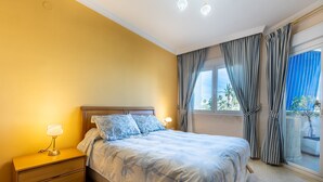A bedroom with a bed, nightstand, lamp, curtains, and a window with a view. - Beautiful Apartment Costa Lago on the Beach with Pool, Wi-Fi & Sea View; Parking Available (Torremolinos)