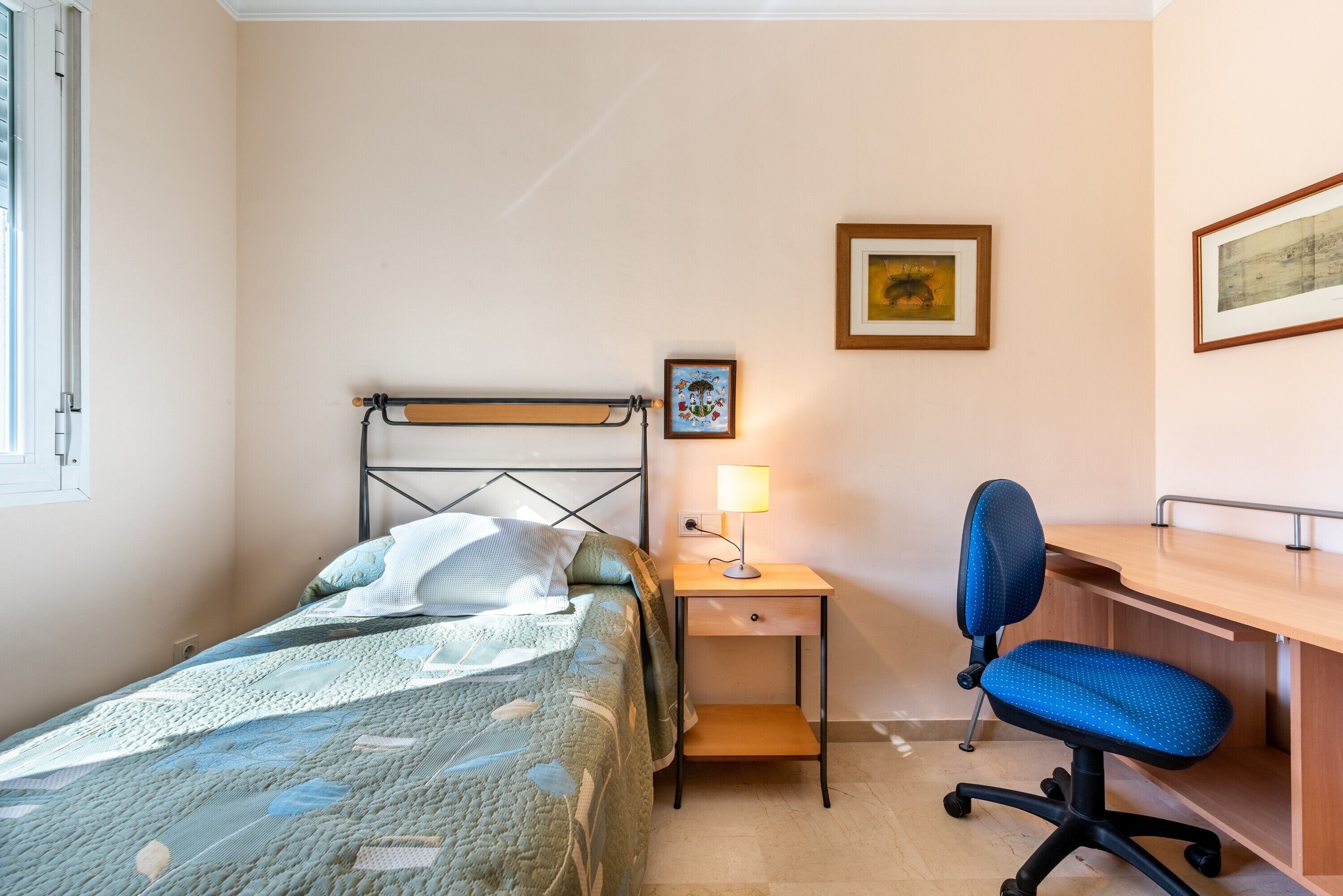 A bedroom with a bed, a desk, a chair, and a lamp.