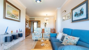 A living room with a blue sofa, floral armchairs, a coffee table, and a clear TV stand with speakers. - Beautiful Apartment Costa Lago on the Beach with Pool, Wi-Fi & Sea View; Parking Available (Torremolinos)