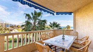 A balcony with a table and chairs, a view of the ocean, and palm trees. - Beautiful Apartment Costa Lago on the Beach with Pool, Wi-Fi & Sea View; Parking Available (Torremolinos)
