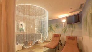 A room with two sun loungers, a decorative light installation, a mounted TV, and a mural of palm trees. - Charming Apartment "Sahara" in Villa Anina with Pool (Klobenstein Ritten)