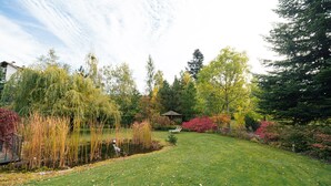Een verzorgde tuin met gazon, vijver en diverse bomen en struiken.