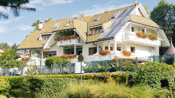 Een twee verdiepingen tellend huis met een schuin dak, zonnepanelen en bloembakken op de balkons.