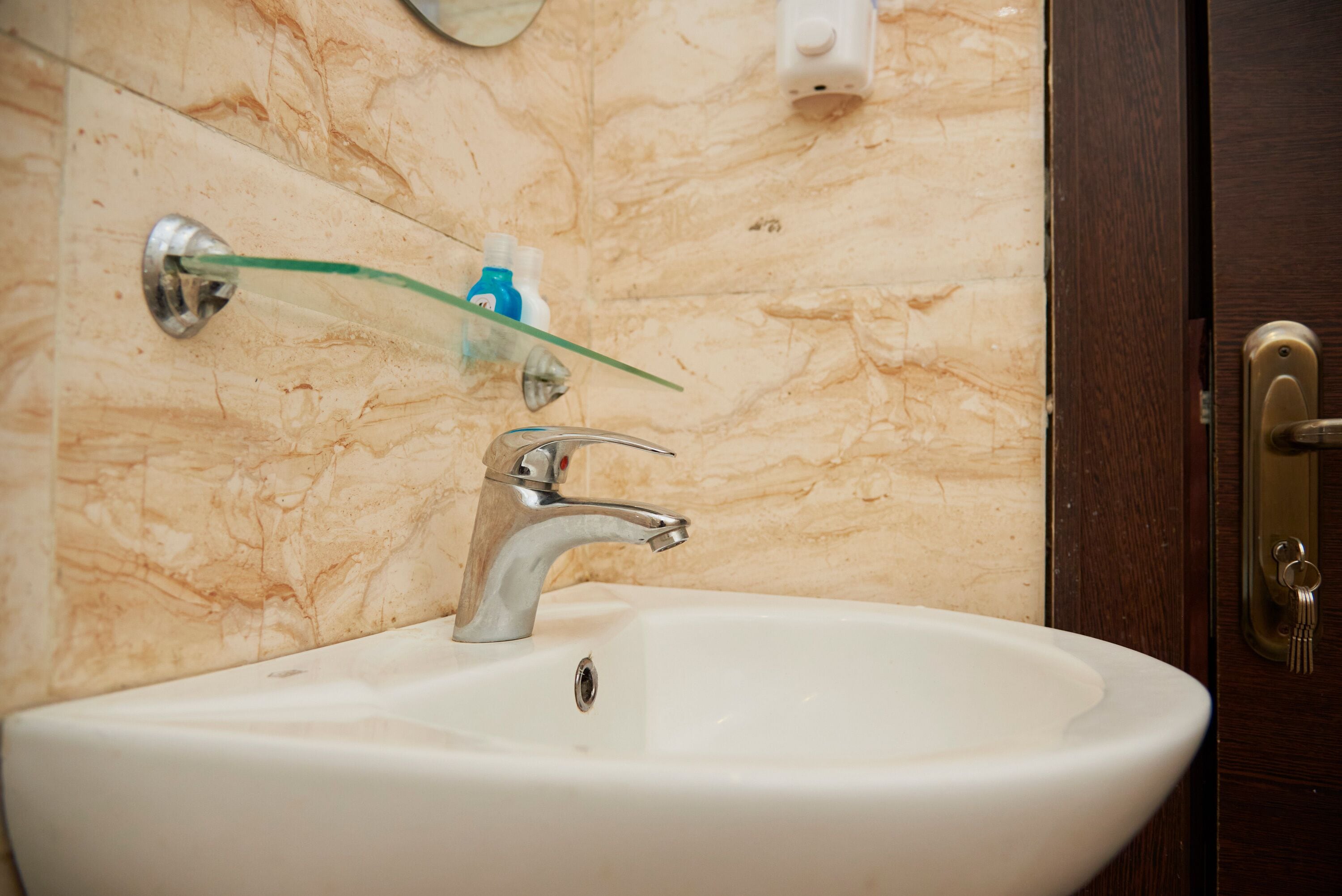 A bathroom with a white sink, a glass shower enclosure, and a marble wall.