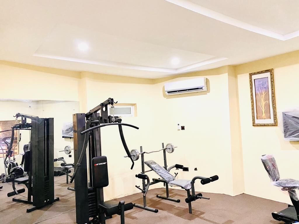 A gym with various exercise machines, an air conditioning unit on the wall, and a framed picture.