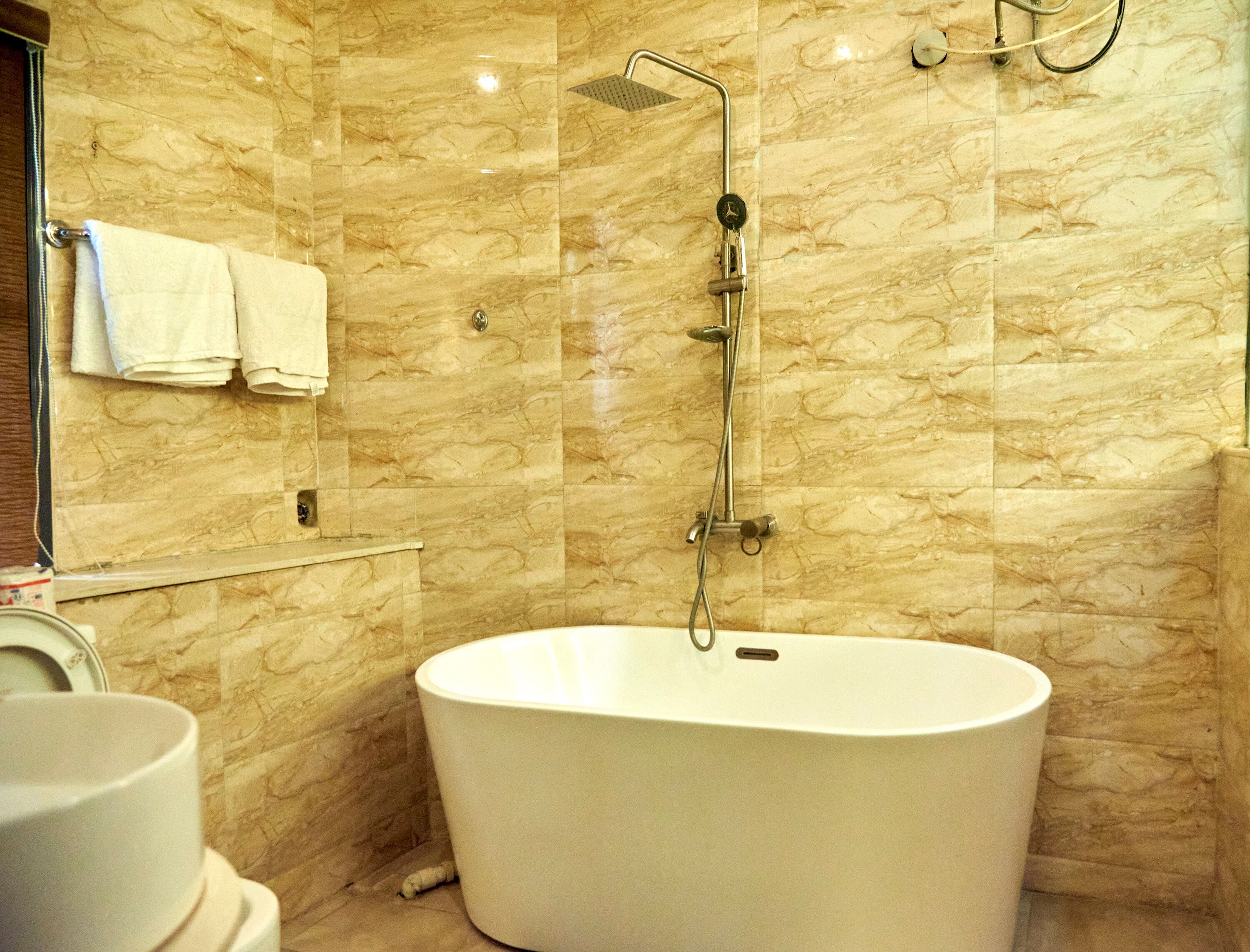 A bathroom with a freestanding bathtub, a showerhead, and a towel rack with towels.