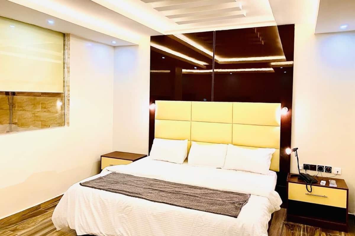Une chambre d’hôtel moderne avec un grand lit, une table de chevet avec une lampe et une fenêtre donnant sur un beau paysage.