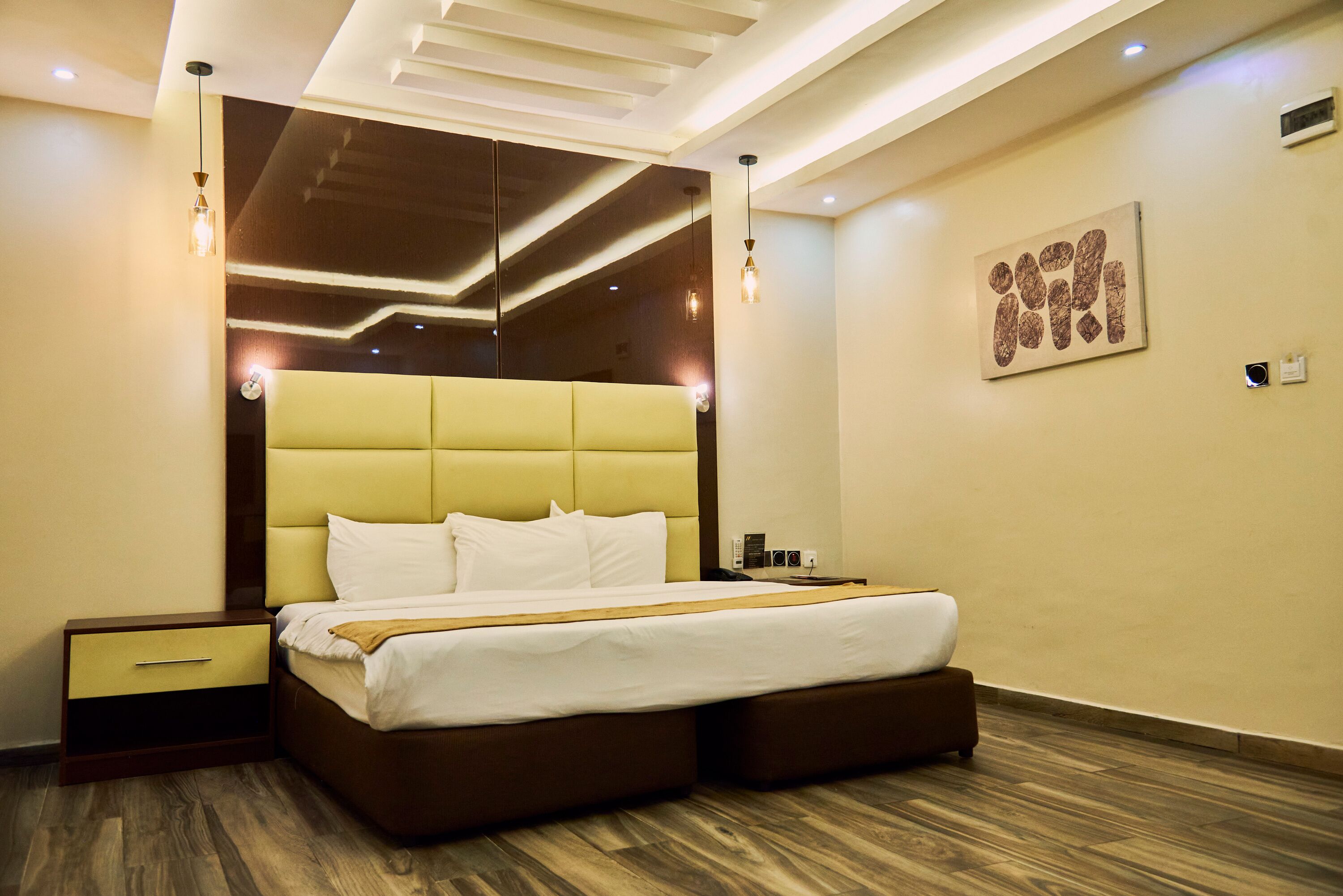 A modern hotel room with a large bed, wooden flooring, and a contemporary ceiling design.