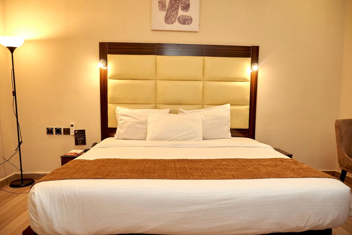 Une chambre d’hôtel avec un grand lit, une tête de lit dotée d’un éclairage intégré, une table de chevet et une lampe sur pied.