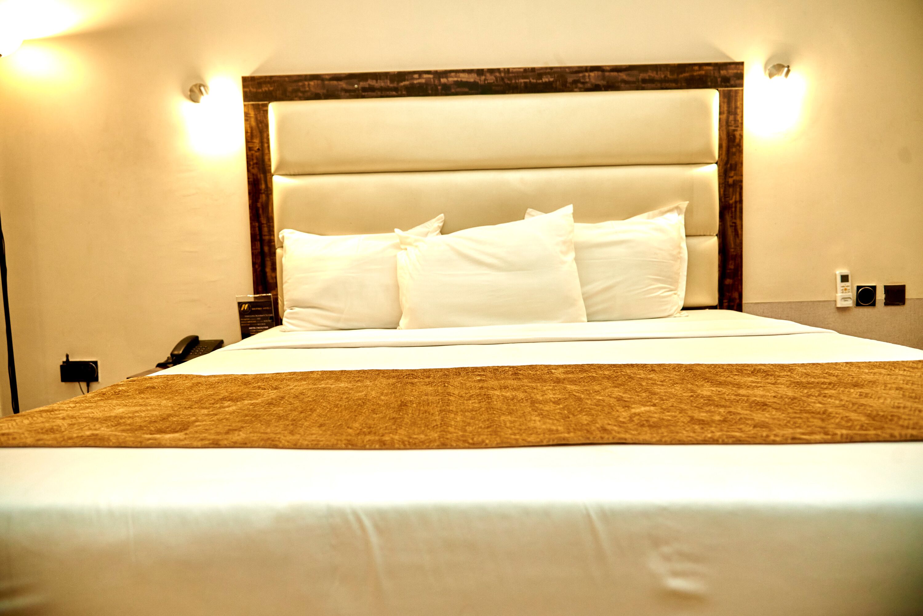 A neatly made bed with white linens and a brown throw blanket.