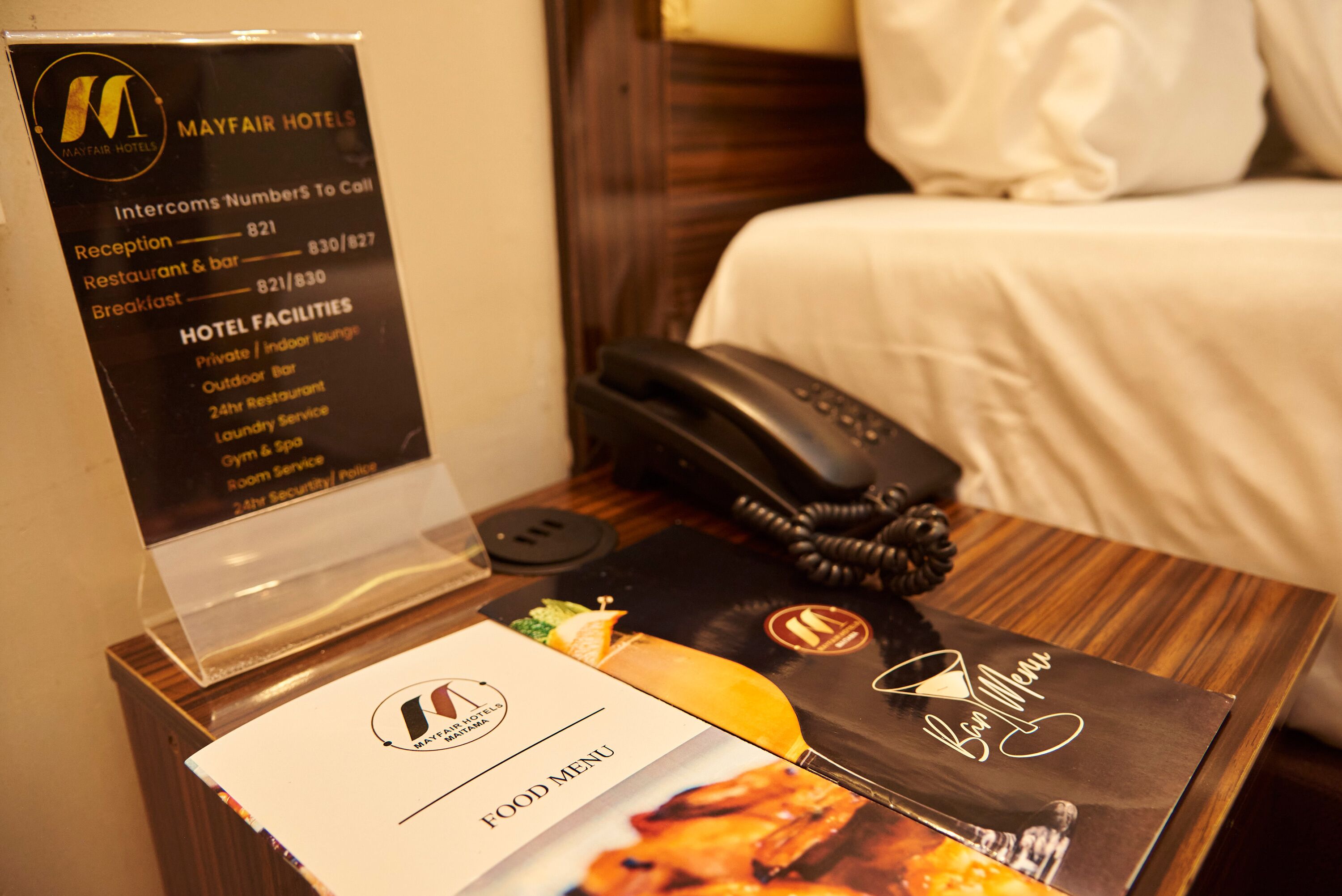 Une chambre d’hôtel comprenant un lit, une table de chevet avec un téléphone, un menu et un panneau indiquant les équipements de l’hôtel.