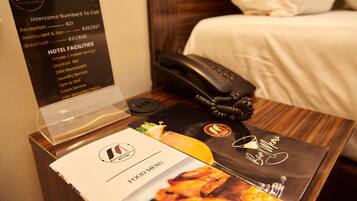 Une chambre d’hôtel comprenant un lit, une table de chevet avec un téléphone, un menu et un panneau indiquant les équipements de l’hôtel.
