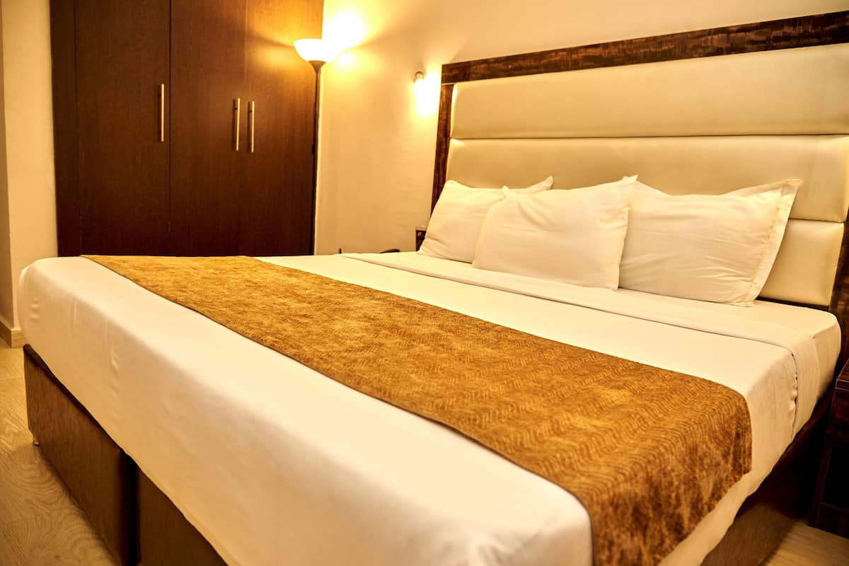 Une chambre d’hôtel avec un grand lit, une armoire en bois et un luminaire fixé au mur.