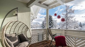 A cozy balcony with a hanging chair, a table with a red cloth, and a view of snow-covered trees. - Charming, Small Ocean Apartment in Villa Anina with Pool (Klobenstein Ritter)
