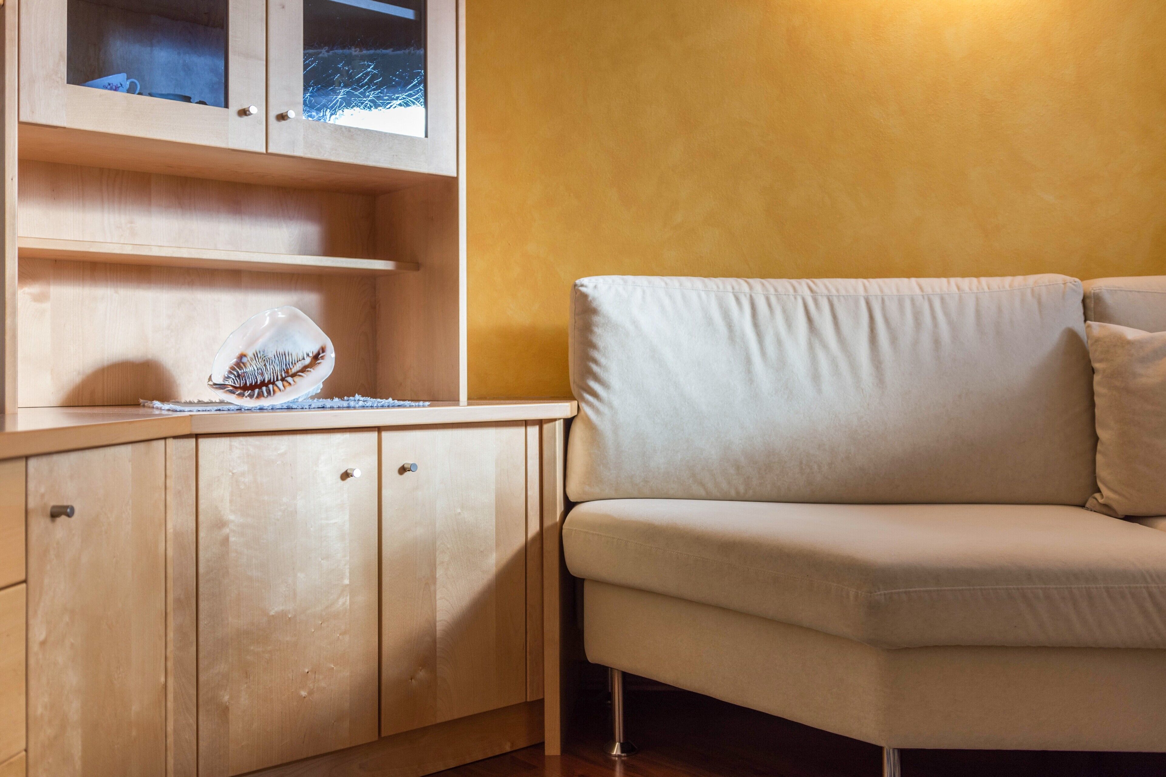 Une pièce comprenant un meuble en bois, un canapé beige et un meuble vitré dans lequel est exposé un objet décoratif.