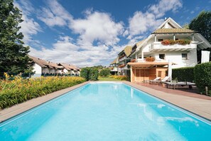 A swimming pool with a clear blue sky, surrounded by lush greenery and a white building with balconies. - Charming Apartment Tundra in Villa Anina with Pool (Klobenstein / Ritten)