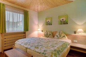 A room with a bed, a bench, a window with curtains, two wall-mounted lamps, and two flower paintings. - Charming Apartment Tundra in Villa Anina with Pool (Klobenstein / Ritten)