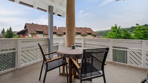 A covered outdoor area with a round table and chairs, a white railing, and a view of houses in the background. - Charming Apartment Tundra in Villa Anina with Pool (Klobenstein / Ritten)