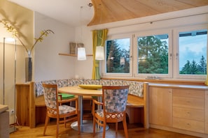Un coin repas accueillant, avec une table en bois, des chaises et une vue sur les arbres à travers de grandes fenêtres.