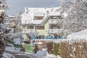 A multi-story building with balconies, a snow-covered roof, and a gated entrance. - Charming Apartment Tundra in Villa Anina with Pool (Klobenstein / Ritten)