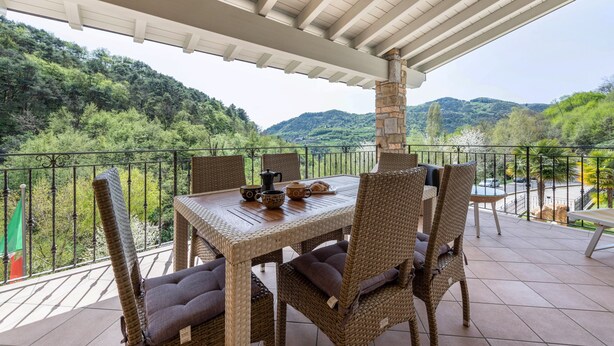 A covered patio with wicker furniture, a table set with dishes, and a view of a green hillside.