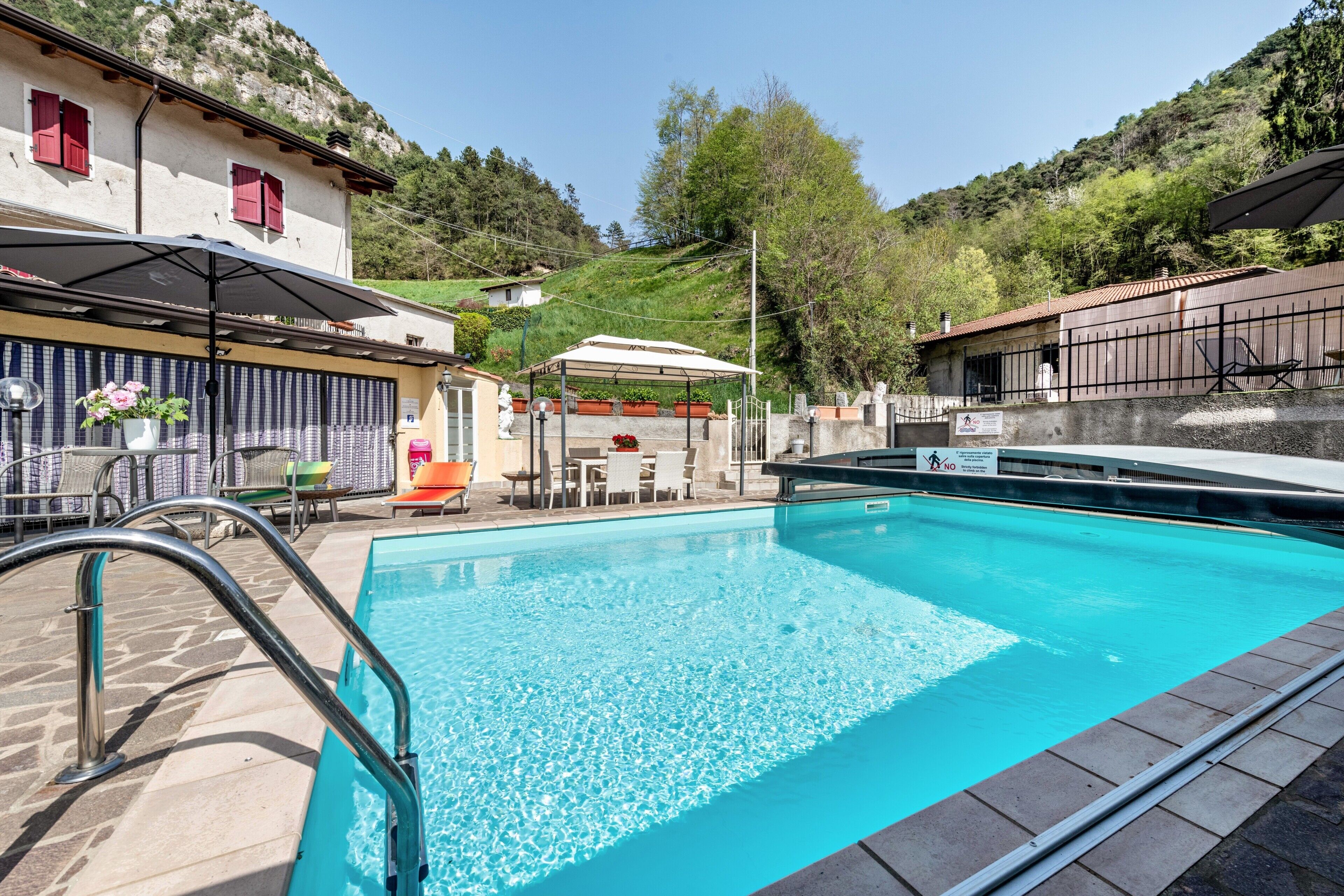 Ein Swimmingpool mit Sonnenschirm, Liegestühlen und Blick auf eine Hügelkette.
