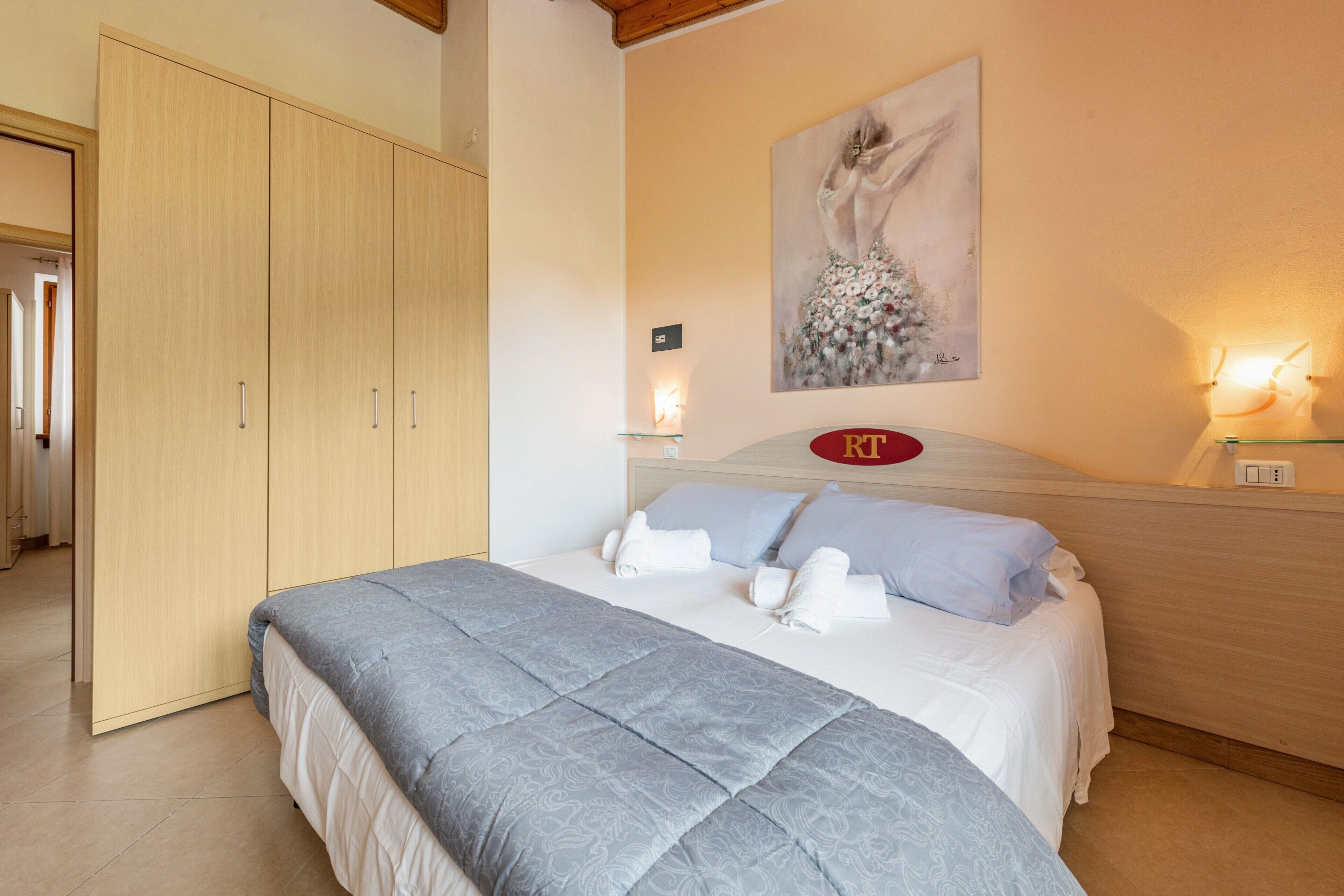 Un dormitorio con cama, armario, un cuadro y una lámpara en la pared.