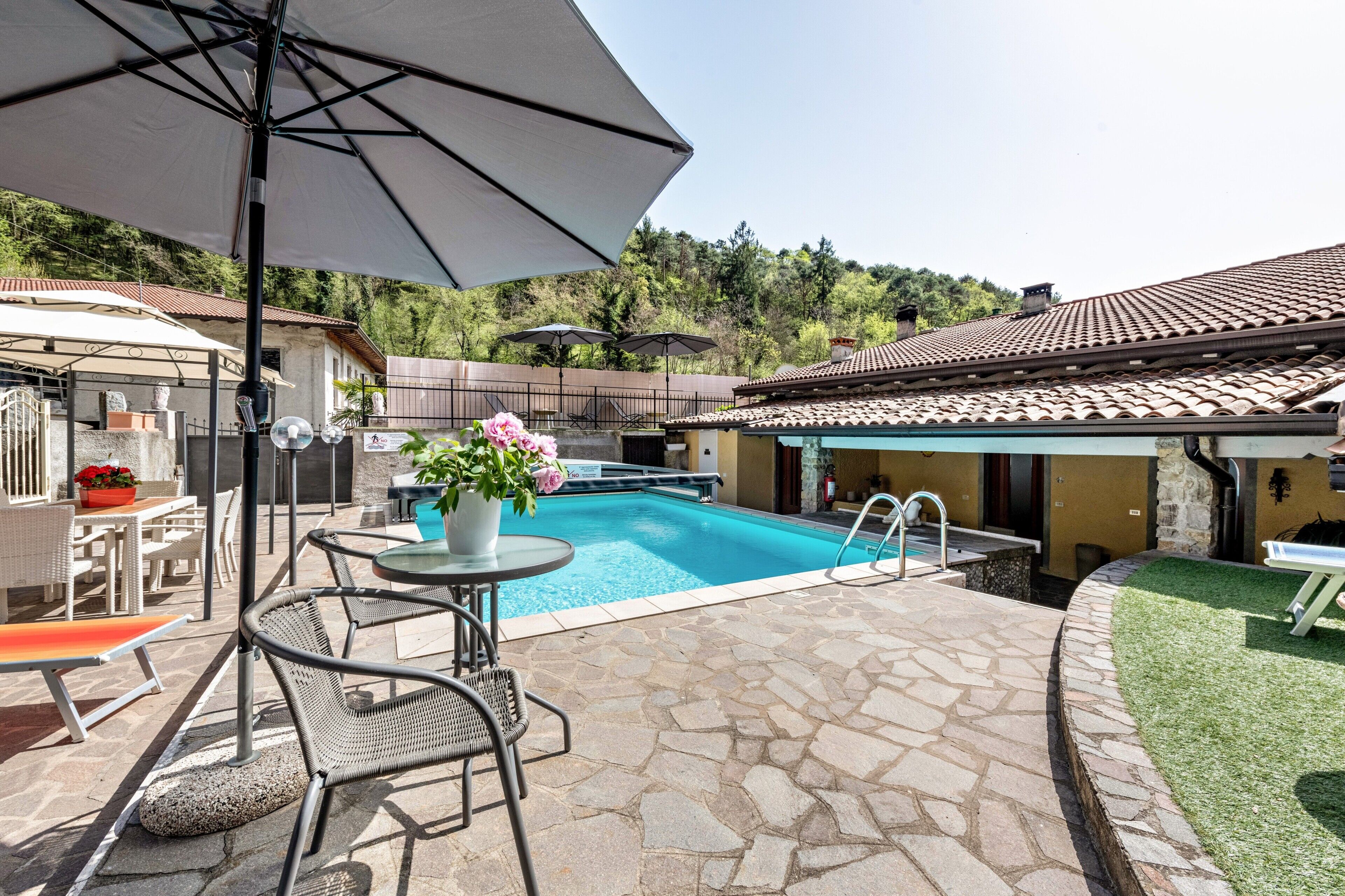 A swimming pool with lounge chairs and umbrellas, surrounded by stone flooring and a small garden.