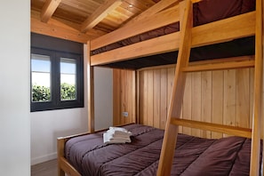Habitación con literas, vigas de madera, una ventana con vistas y una cama con colcha marrón.