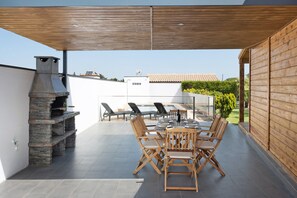 Een terras buiten met een stenen open haard, houten meubels en uitzicht op de omgeving.