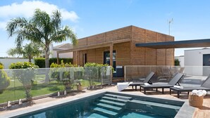 Un'area piscina moderna con un solarium in legno, lettini e una recinzione in vetro trasparente.