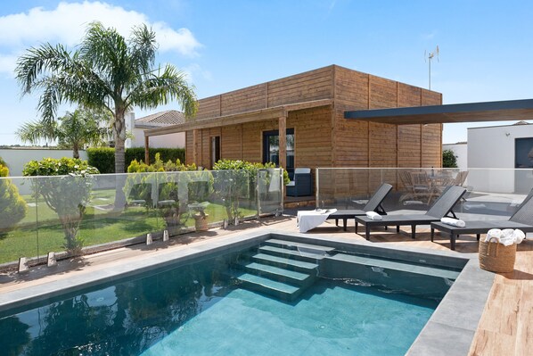 Een modern zwembadgedeelte met een houten terras, ligbedden en een glazen omheining.