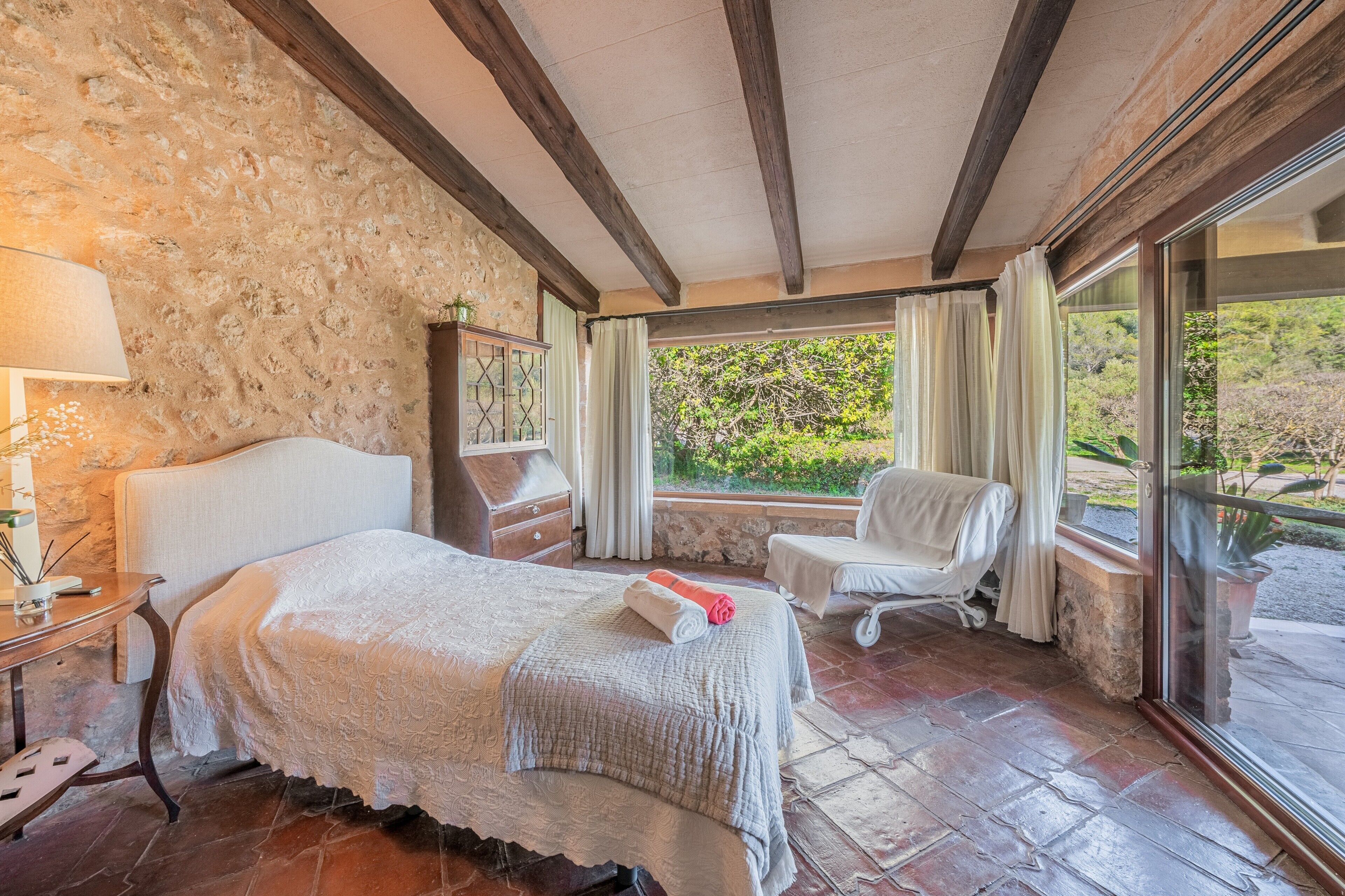 A room with a bed, a chair, a table, and a window with curtains.