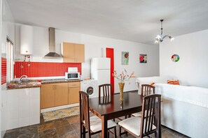 Una cuina moderna amb un respatller vermell, una zona de menjador amb taula i cadires de fusta, un sofà blanc i una petita catifa.